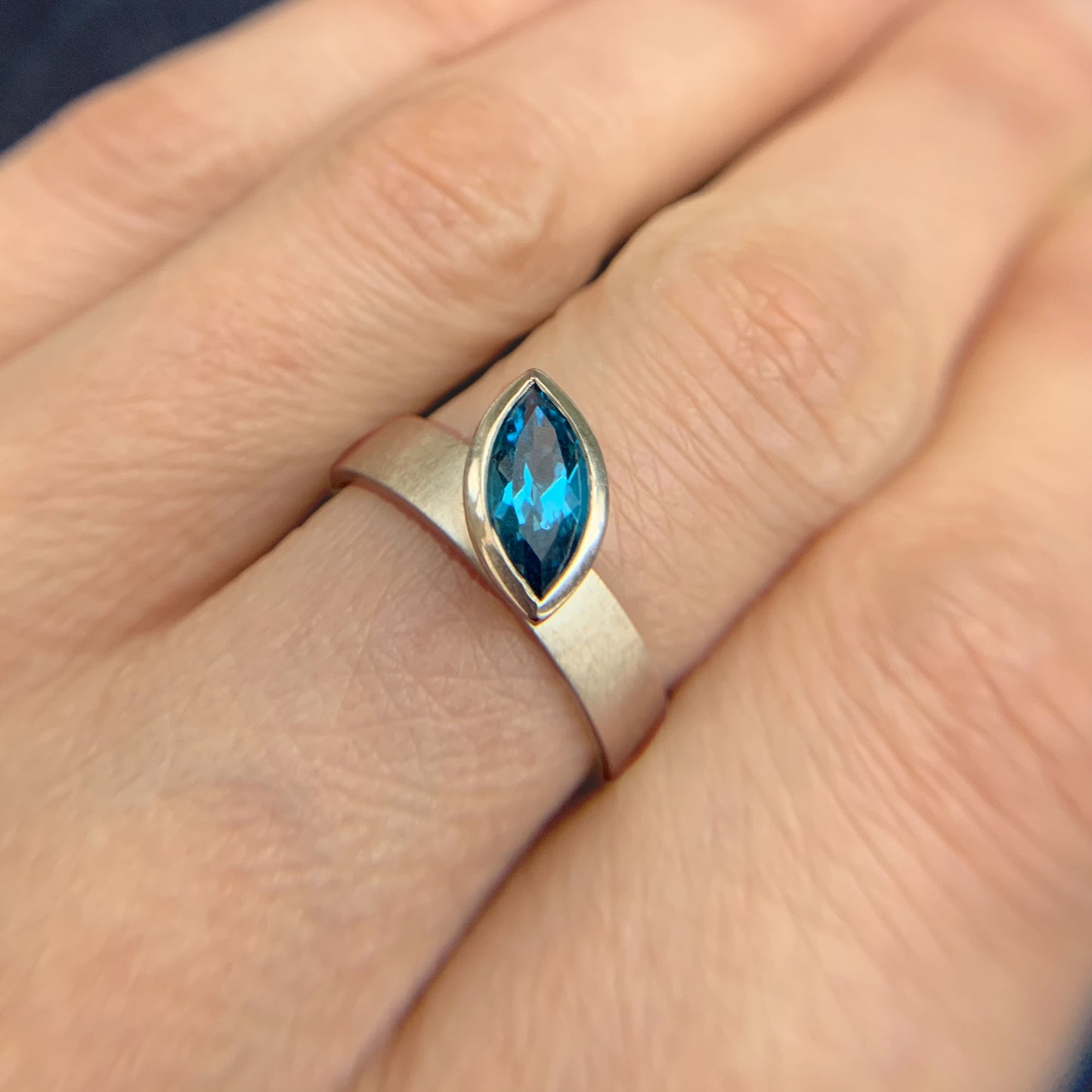 Kate Phipps Jewellery Solitaire ring marquise Swiss blue topaz offset from wide silver band at an angle model photo 2