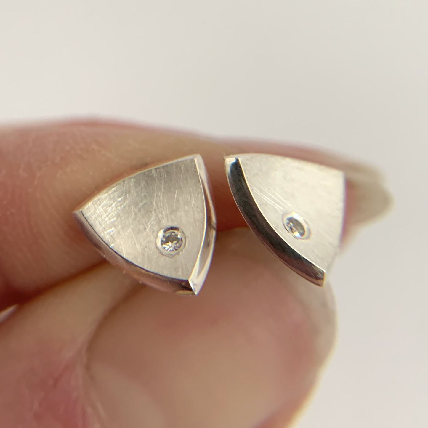 Kate Phipps Jewellery Trillion stud earrings medium silver with flush set diamonds held in hand